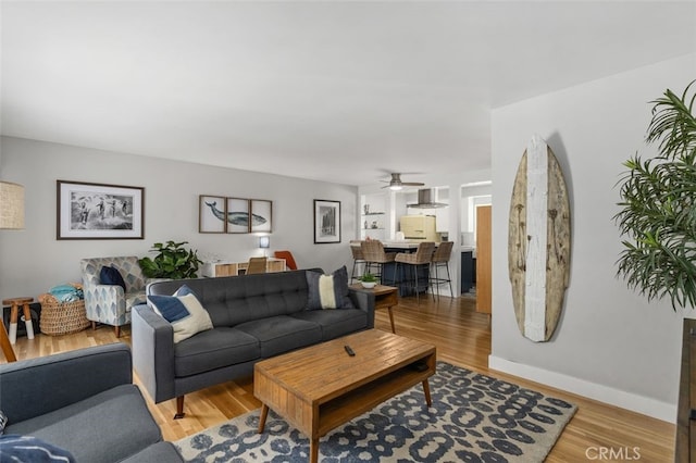 living room featuring ceiling fan, light wood-style floors, and baseboards
