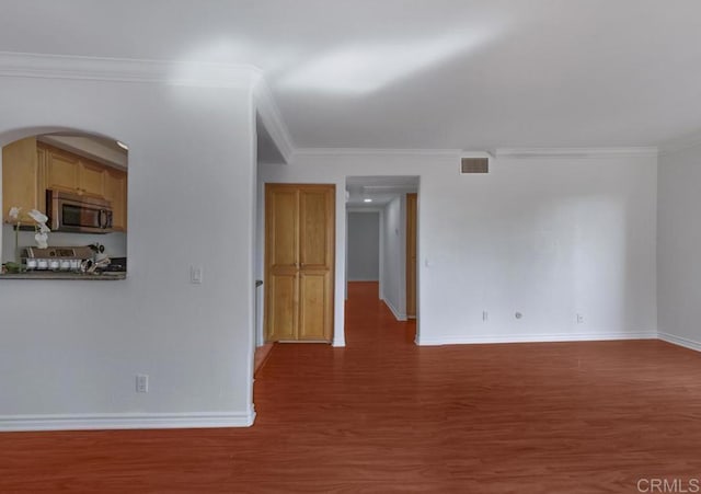 empty room featuring visible vents, arched walkways, wood finished floors, baseboards, and ornamental molding