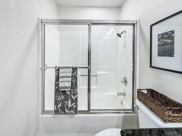 bathroom with bath / shower combo with glass door, a textured wall, and toilet