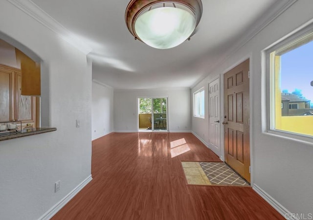 entrance foyer with crown molding, arched walkways, baseboards, and wood finished floors