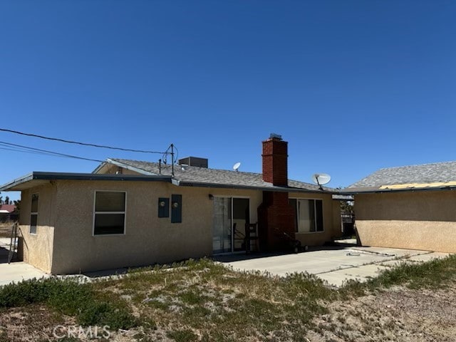 rear view of house with a chimney, a patio area, and stucco siding