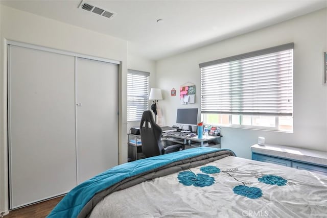 bedroom with visible vents, multiple windows, a closet, and wood finished floors