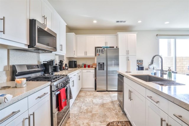 kitchen with light stone counters, white cabinetry, visible vents, stainless steel appliances, and a sink