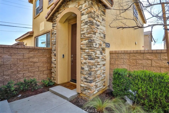 entrance to property with stucco siding, stone siding, and fence
