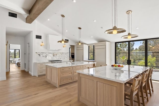 kitchen featuring tasteful backsplash, light stone countertops, beam ceiling, light wood finished floors, and a large island with sink