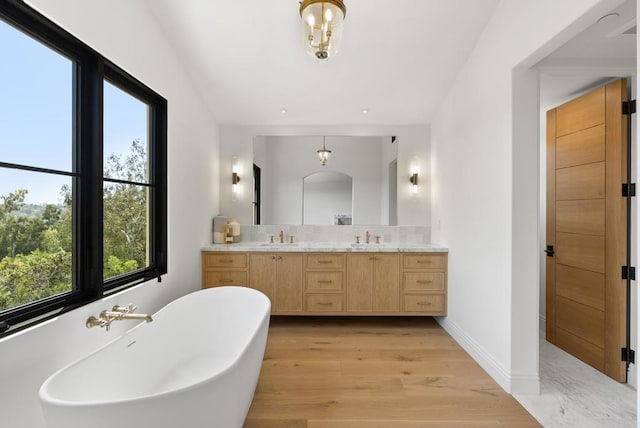 bathroom with a freestanding bath, double vanity, a sink, and wood finished floors