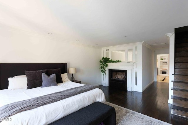 bedroom featuring a fireplace, baseboards, ornamental molding, and wood finished floors