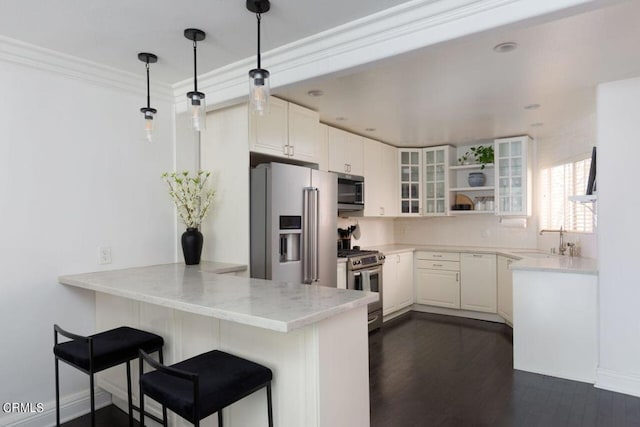 kitchen featuring glass insert cabinets, a sink, appliances with stainless steel finishes, a kitchen bar, and a peninsula