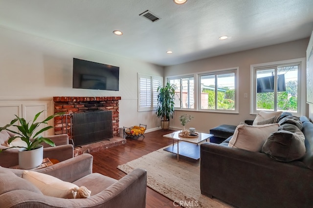 living room featuring wood finished floors, a brick fireplace, visible vents, and recessed lighting
