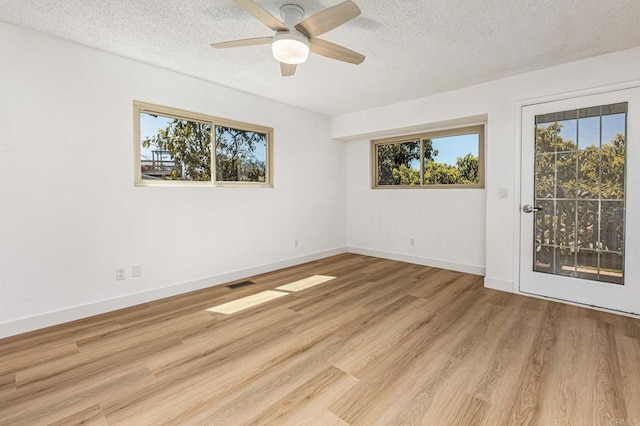 spare room featuring light wood-style flooring, ceiling fan, visible vents, and a wealth of natural light