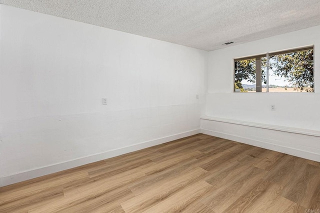 unfurnished room with light wood finished floors, visible vents, a textured ceiling, and baseboards