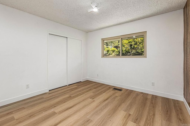 empty room with light wood-style floors, baseboards, visible vents, and a textured ceiling