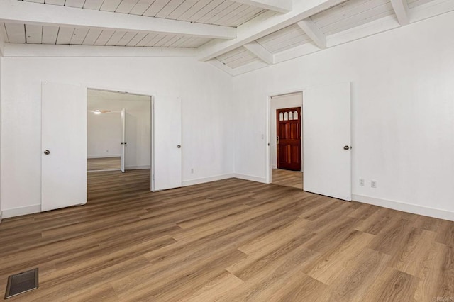 empty room featuring baseboards, visible vents, light wood-type flooring, and vaulted ceiling with beams