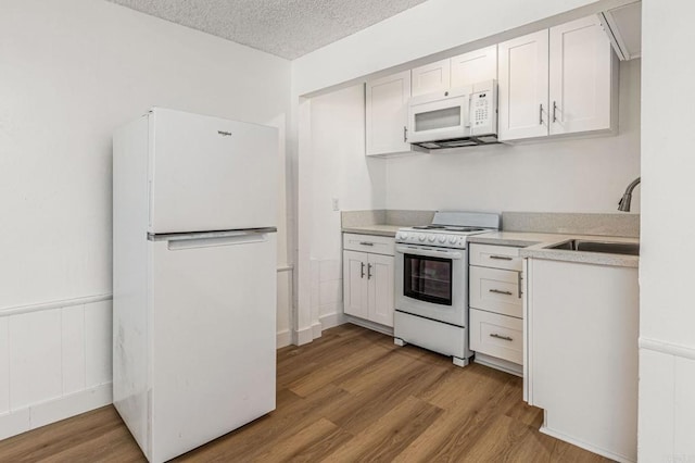 kitchen featuring a sink, white appliances, wood finished floors, and a textured ceiling