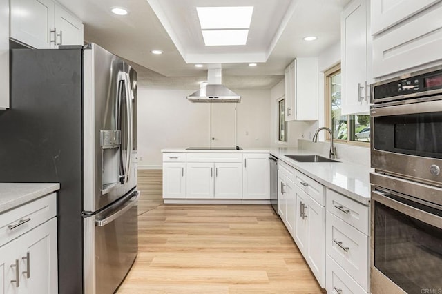 kitchen with stainless steel appliances, white cabinets, island range hood, light wood finished floors, and a sink