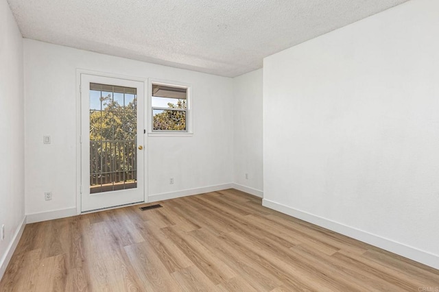 empty room with light wood-type flooring, baseboards, and a textured ceiling