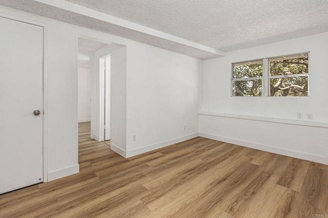 empty room featuring light wood-style flooring, baseboards, and a textured ceiling