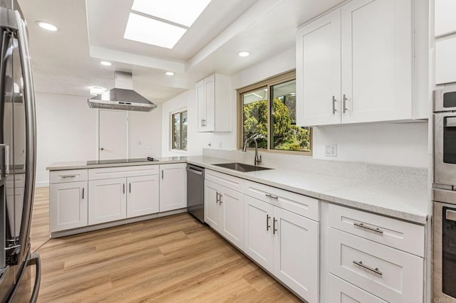 kitchen featuring light wood-style flooring, white cabinets, wall chimney exhaust hood, appliances with stainless steel finishes, and a sink