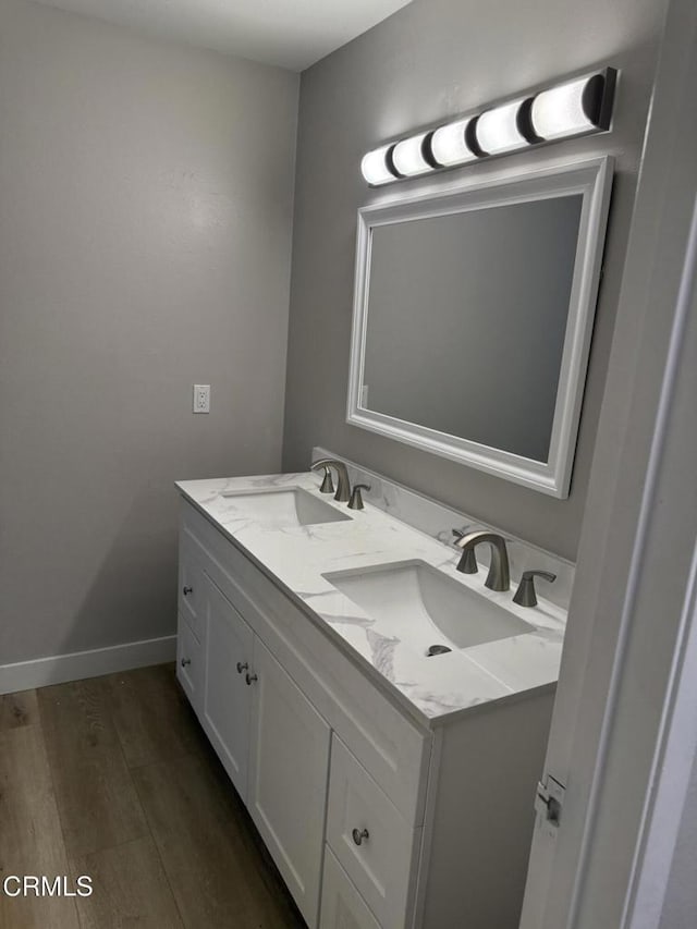 bathroom with wood finished floors, double vanity, a sink, and baseboards