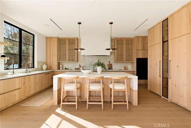 kitchen with light brown cabinetry, glass insert cabinets, a center island, light wood-style flooring, and backsplash
