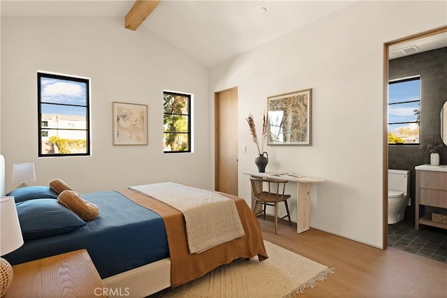 bedroom with connected bathroom, lofted ceiling with beams, wood finished floors, and visible vents