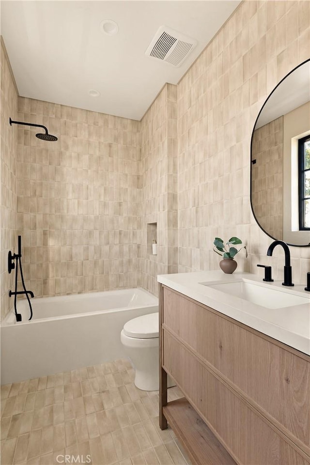full bathroom with visible vents, vanity, bathing tub / shower combination, toilet, and tile walls
