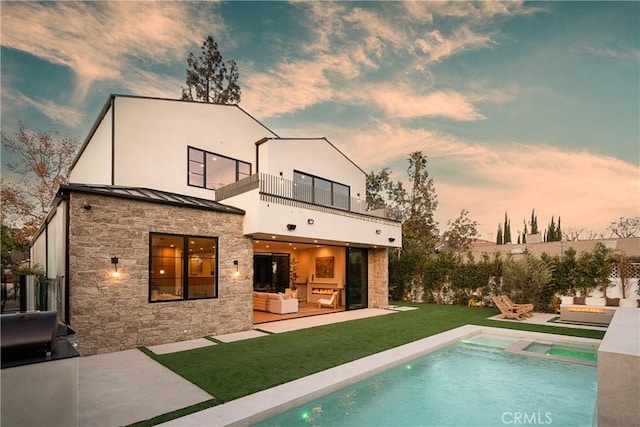 back of property at dusk featuring an outdoor hangout area, a patio, stone siding, and a balcony