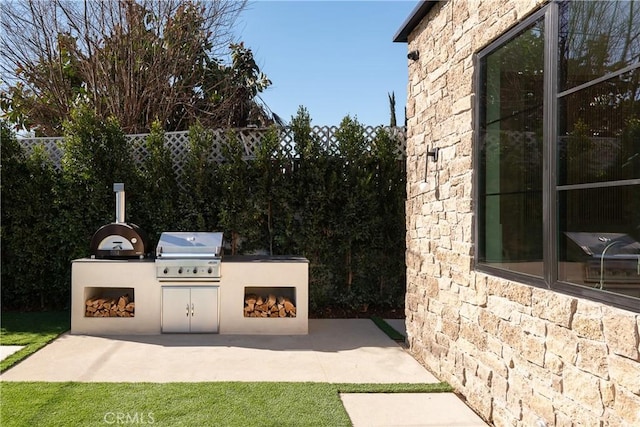 view of patio featuring an outdoor fireplace, fence, and a grill