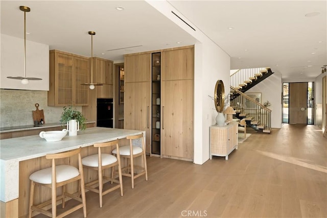 kitchen with light wood finished floors, a kitchen breakfast bar, brown cabinetry, visible vents, and modern cabinets
