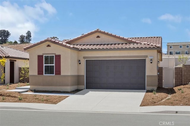 mediterranean / spanish house with fence, a tile roof, concrete driveway, a garage, and stucco siding