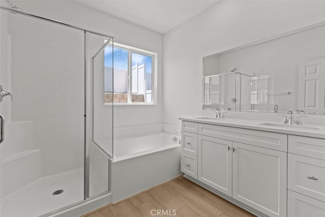 full bath with double vanity, wood finished floors, a sink, a bath, and a shower stall