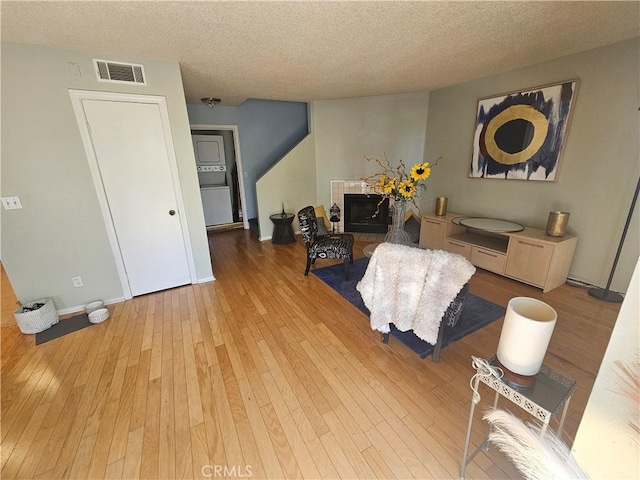living room with a textured ceiling, visible vents, light wood-style flooring, and baseboards