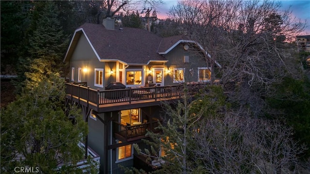 rear view of property with a shingled roof, a deck, and a chimney