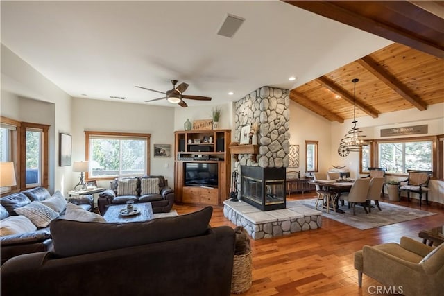 living area with wooden ceiling, a stone fireplace, ceiling fan, beamed ceiling, and wood-type flooring