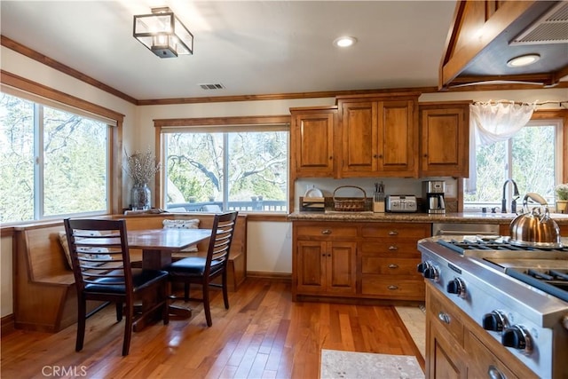 kitchen with crown molding, light wood-type flooring, visible vents, stainless steel gas cooktop, and brown cabinets