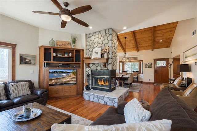 living area with visible vents, a stone fireplace, wood finished floors, and ceiling fan