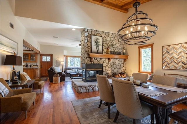 813 Brentwood Dr, Lake Arrowhead, CA 92352 - dining area featuring a chandelier, hardwood / wood-style flooring, a stone fireplace, a high ceiling, and ceiling fan