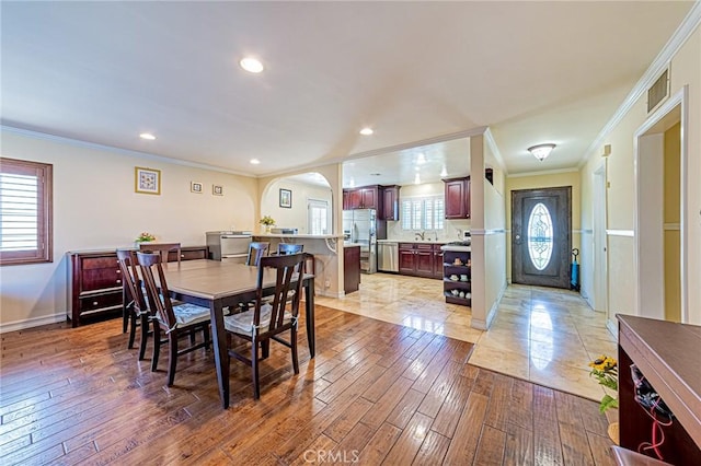 dining space featuring ornamental molding, arched walkways, baseboards, recessed lighting, and light wood-type flooring