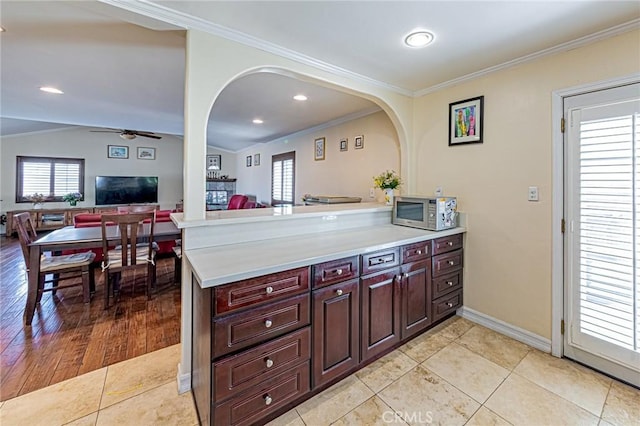 kitchen featuring stainless steel microwave, light countertops, crown molding, a ceiling fan, and a peninsula