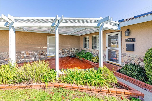 view of exterior entry featuring stone siding, stucco siding, and a pergola