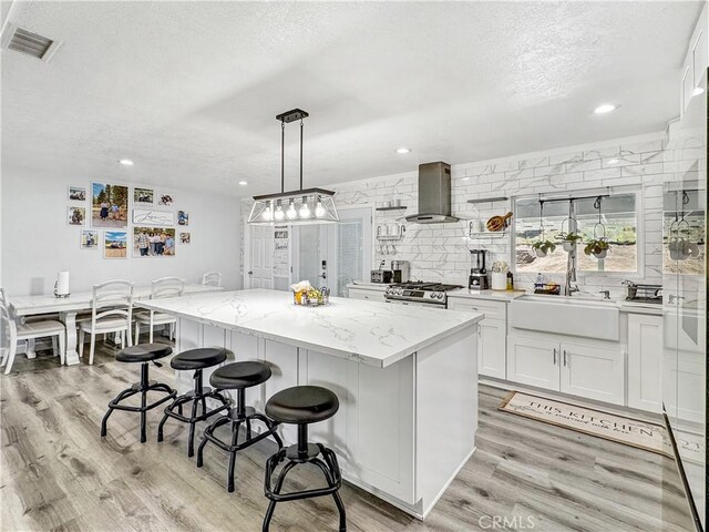7455 Bangor Ave, Hesperia, CA 92345 - kitchen featuring visible vents, wall chimney range hood, a kitchen bar, a textured ceiling, and a sink