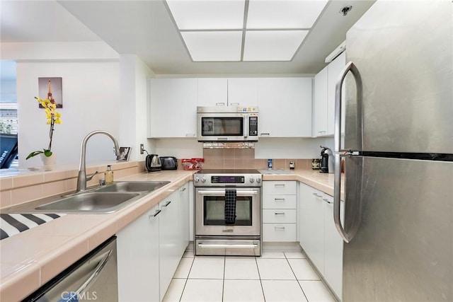 kitchen with appliances with stainless steel finishes, light tile patterned flooring, a sink, and white cabinets