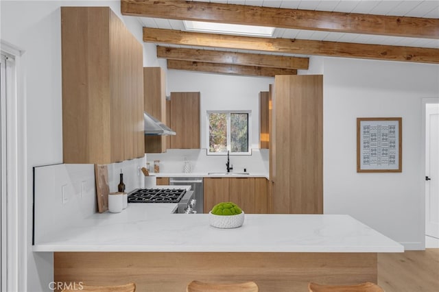 kitchen with modern cabinets, a sink, light countertops, under cabinet range hood, and brown cabinets