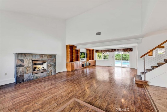 25 Bennington, Irvine, CA 92620 - unfurnished living room with a towering ceiling, a tiled fireplace, stairway, visible vents, and wood-type flooring