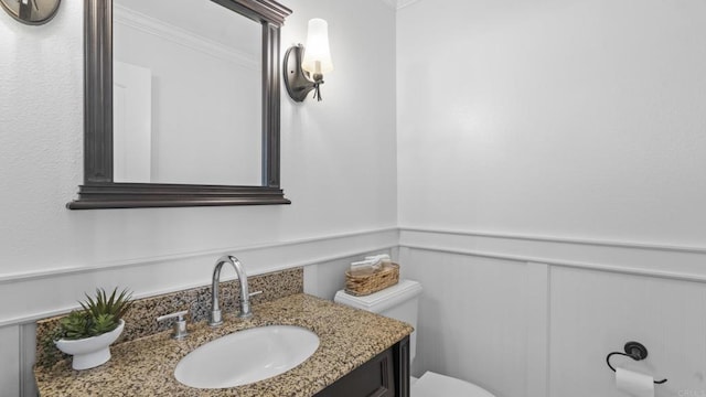 bathroom featuring vanity, crown molding, a decorative wall, toilet, and a wainscoted wall