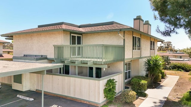 exterior space with a chimney, a balcony, and stucco siding