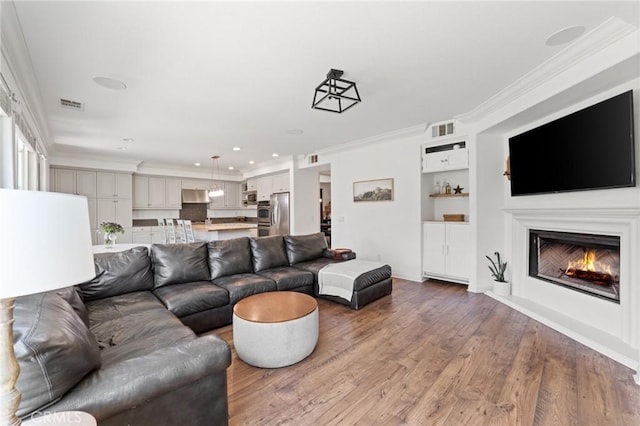 living room with a lit fireplace, wood finished floors, visible vents, and ornamental molding