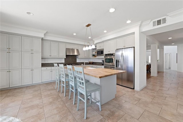 kitchen featuring visible vents, appliances with stainless steel finishes, butcher block counters, under cabinet range hood, and ornamental molding