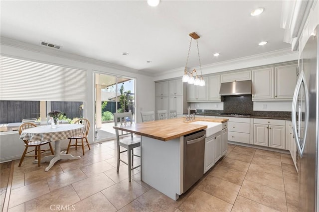 kitchen with a sink, under cabinet range hood, backsplash, appliances with stainless steel finishes, and an island with sink