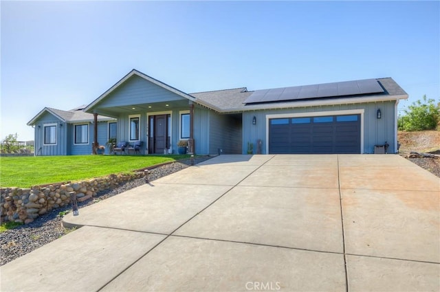 ranch-style house featuring a front yard, board and batten siding, roof mounted solar panels, an attached garage, and driveway
